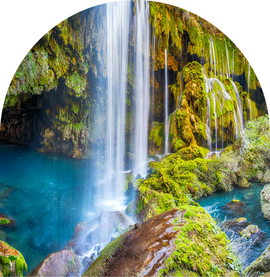 A vibrant waterfall cascades into a clear blue pool surrounded by mossy rocks.